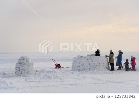 Family with children near unfinished Igloo, a national shelter from the cold, made of snow bricks 125733842