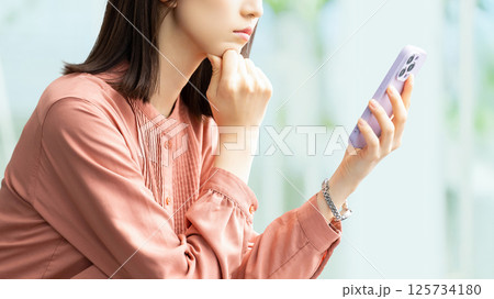 スマートフォンを見て考える女性・ビジネスウーマン スマートフォンを見て考える女性・ビジネスウーマン 125734180