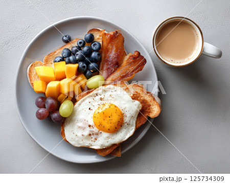 Breakfast toast with fried egg, bacon, fresh fruit, and coffee on gray plate, colorful and appetizing morning meal 125734309