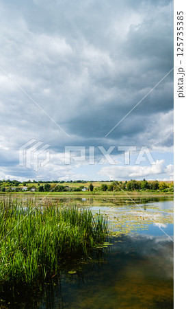 Rural landscape, rain clouds over the pond, vertical photo Rural landscape, rain clouds over the pond, vertical photo 125735385
