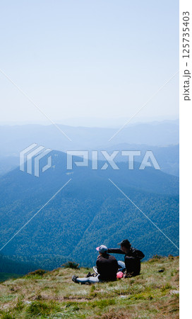 Two people sitting on top of a mountain and looking at the landscape in summer 125735403