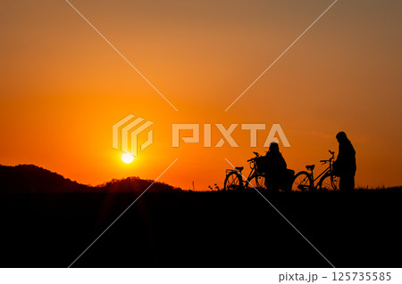 夕日を背景に女性と自転車のシルエット 夕日を背景に女性と自転車のシルエット 125735585