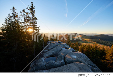 Scenic sunrise at Pysanyi Kamin in Carpathians, Ukraine. Rocky surface in foreground. Breathtaking view of rolling hills, dense forests, and distant mountains illuminated by soft morning light. 125735827