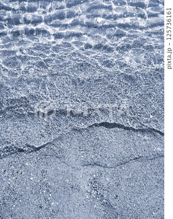 Beautiful small sea waves of clean transparent water on the sandy beach of sea shore on sunny day. Clean water, sun glare and shadows on sandy bottom close-up. Natural abstract background. 125736161