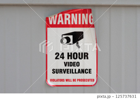 Peeling video surveillance warning sign affixed to weathered concrete wall surface Peeling video surveillance warning sign affixed to weathered concrete wall surface 125737631