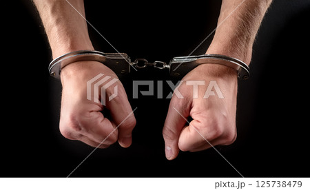 手錠をかけられた両手のクローズアップ ／ 犯罪や拘束、法的テーマを示すリアルな表現素材 125738479