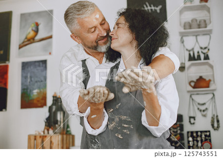 Mutual creative work. Adult elegant couple in casual clothes and aprons. People creating a bowl on a pottery wheel in a clay studio. 125743551