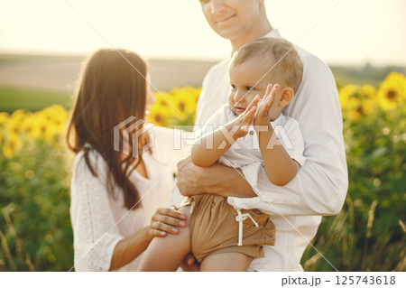 Photo of a young family at the sunflowers field on a sunny day. Brunette mother, father and their little blonde son posing for a photo. Man and woman hugging their son. Photo of a young family at the sunflowers field on a sunny day. Brunette mother, father and their little blonde son posing for a photo. Man and woman hugging their son. 125743618