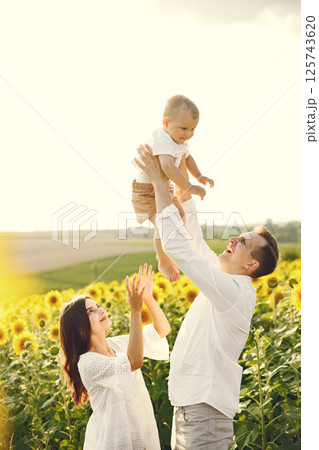 Photo of a young family at the sunflowers field on a sunny day. Brunette mother, father and their little blonde son posing for a photo. Man and woman playing with their son. Photo of a young family at the sunflowers field on a sunny day. Brunette mother, father and their little blonde son posing for a photo. Man and woman playing with their son. 125743620