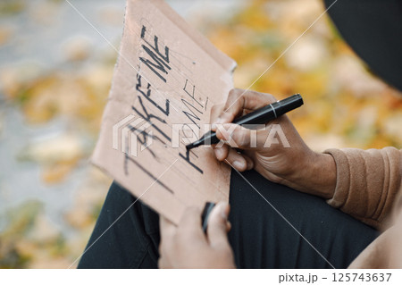 Focus on a cardboard sign. Young black man hitchhiking on road and holding a sign take me home. Male traveler traveling alone by autostop. Focus on a cardboard sign. Young black man hitchhiking on road and holding a sign take me home. Male traveler traveling alone by autostop. 125743637