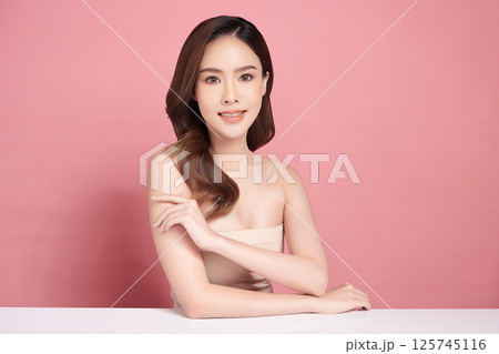 A beautiful young Asian woman with clean, fresh skin against a pink background. Skincare, facial treatment, cosmetology, beauty, and spa. An elegant portrait of an Asian woman. 125745116