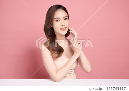A beautiful young Asian woman with clean, fresh skin against a pink background. Skincare, facial treatment, cosmetology, beauty, and spa. An elegant portrait of an Asian woman. A beautiful young Asian woman with clean, fresh skin against a pink background. Skincare, facial treatment, cosmetology, beauty, and spa. An elegant portrait of an Asian woman. 125745117