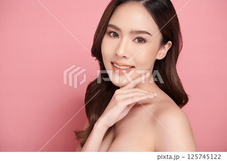 A beautiful young Asian woman with clean, fresh skin against a pink background. Skincare, facial treatment, cosmetology, beauty, and spa. An elegant portrait of an Asian woman. 125745122