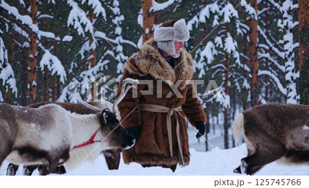 Breeder walking with reindeer in snowy forest 125745766