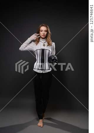 Elegant woman in corset holding skull gazes confidently in dark studio 125746641