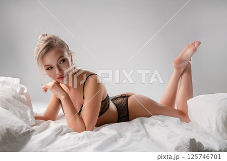 Beautiful woman poses in lingerie on a bed with a soft white backdrop Beautiful woman poses in lingerie on a bed with a soft white backdrop 125746701