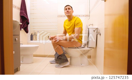 Man sitting on toilet finishing toilet paper roll and yelling Man sitting on toilet finishing toilet paper roll and yelling 125747235