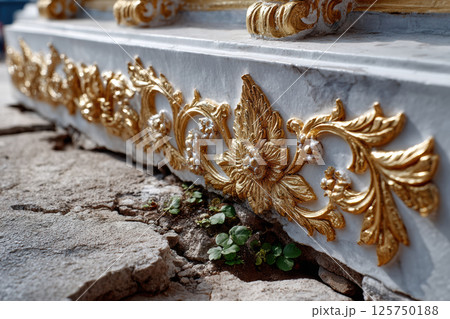 Ornate gold decorative detail with floral motifs adorns marble surface, contrasting with cracked stone and small plants growing beneath. intricate design adds elegance to scene Ornate gold decorative detail with floral motifs adorns marble surface, contrasting with cracked stone and small plants growing beneath. intricate design adds elegance to scene 125750188