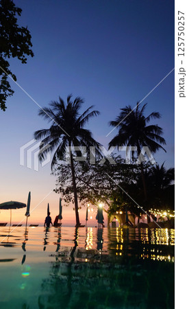 Tourists enjoying sunset at infinity pool overlooking tropical ocean 125750257