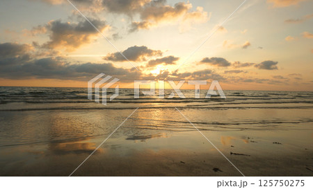 Golden sunset reflecting on wet sandy beach with clouds and waves Golden sunset reflecting on wet sandy beach with clouds and waves 125750275
