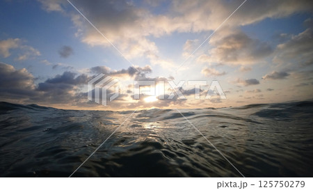 Ocean waves reflecting golden sunset light under cloudy sky Ocean waves reflecting golden sunset light under cloudy sky 125750279