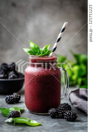 Fresh blackberry smoothie in mason jar with basil leaves and striped straw on dark background. 125751225