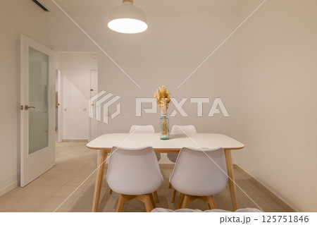 Dining area with vase centerpiece on a white table and four chairs near the apartment entrance Dining area with vase centerpiece on a white table and four chairs near the apartment entrance 125751846