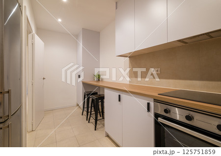 Modern kitchen perspective with bar counter, stools, white cabinetry and wood countertop finish 125751859