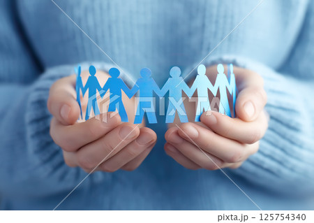 A person holding a paper cutout of a group of people. The concept of unity, teamwork, social connection, and support within a community. Generative AI. 125754340