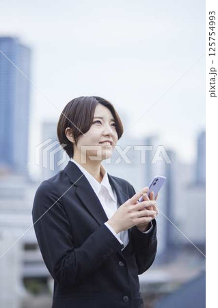 スーツを着た若い日本人女性と都会の街並み スーツを着た若い日本人女性と都会の街並み 125754993