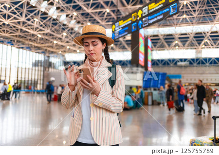 Young Caucasian woman wearing straw hat using smartphone. Digital mobile app for trip. Concept of modern vacation and travel Young Caucasian woman wearing straw hat using smartphone. Digital mobile app for trip. Concept of modern vacation and travel 125755789