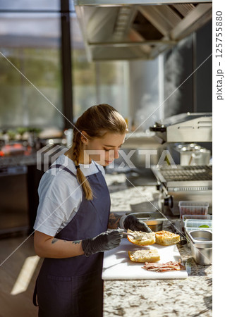 A Young Chef Expertly Preparing a Delicious and Flavorful Sandwich inside a Modern Kitchen 125755880