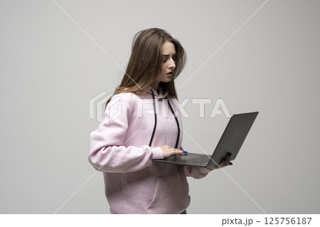 Young brunette woman in hoodie holding laptop and working on blank background 125756187