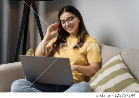Relaxed on the sofa, a woman in eyeglasses switches between freelance tasks, online shopping tabs, and catching up on personal emails Relaxed on the sofa, a woman in eyeglasses switches between freelance tasks, online shopping tabs, and catching up on personal emails 125757144