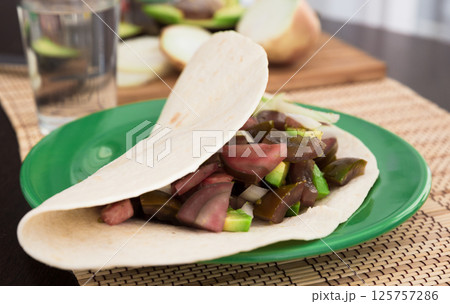 Salad of black tomatoes, avocado and onions in Italian tortilla on green plate 125757286