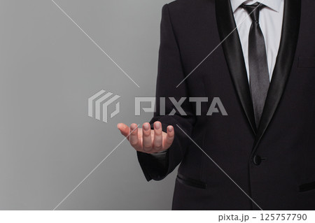 A man in a black suit is holding hand out in a gesture of surrender. 125757790
