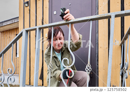 Removing rust from ornate porch railing, cheerful female painter uses wire brush with a smile, enjoying process of restoring metal to clean condition. Removing rust from ornate porch railing, cheerful female painter uses wire brush with a smile, enjoying process of restoring metal to clean condition. 125758502