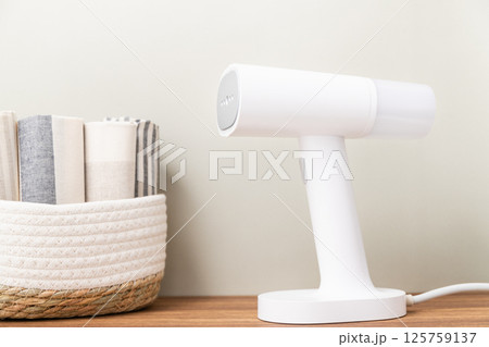 White handheld portable steamer next to laundry basket on table 125759137