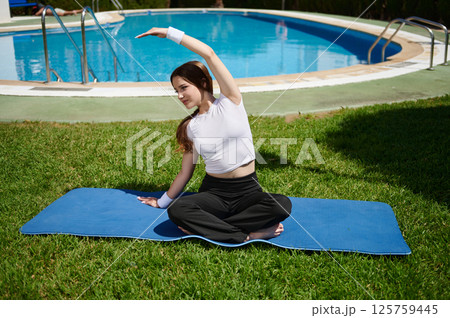 Woman Practicing Yoga Outdoors by a Swimming Pool on a Sunny Day 125759445