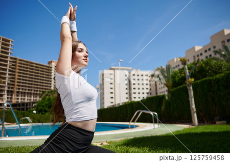 Young Woman Practicing Outdoor Yoga by a Pool Under Clear Blue Skies Young Woman Practicing Outdoor Yoga by a Pool Under Clear Blue Skies 125759458