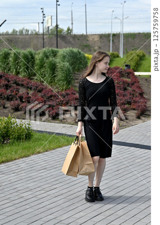 Woman in black dress walking with shopping bags in an outdoor park area. Woman in black dress walking with shopping bags in an outdoor park area. 125759758