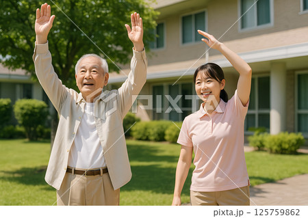 介護施設の庭で高齢男性と介護士が一緒に体操をする様子 125759862