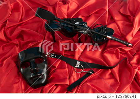 Adult sex games. Kinky lifestyle. Mask and collar, ridding crop high heels on the red linen. Bdsm outfit Adult sex games. Kinky lifestyle. Mask and collar, ridding crop high heels on the red linen. Bdsm outfit 125760241