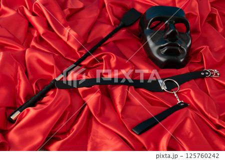 Adult sex games. Kinky lifestyle. Mask and whip ridding crop on the red linen. Bdsm outfit Adult sex games. Kinky lifestyle. Mask and whip ridding crop on the red linen. Bdsm outfit 125760242