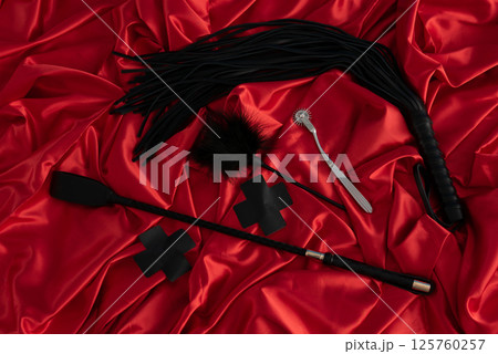 Adult sex games. Kinky lifestyle. Spank and whip ridding crop on the red linen. Bdsm outfit 125760257