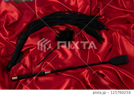Adult sex games. Kinky lifestyle. Spank and whip ridding crop on the red linen. Bdsm outfit 125760258