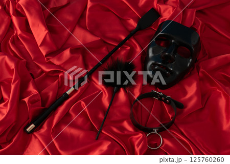 Adult sex games. Kinky lifestyle. Mask and whip ridding crop on the red linen. Bdsm outfit 125760260