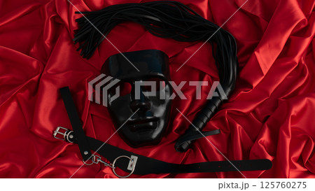 Adult sex games. Kinky lifestyle. Mask and whip ridding crop on the red linen. Bdsm outfit 125760275