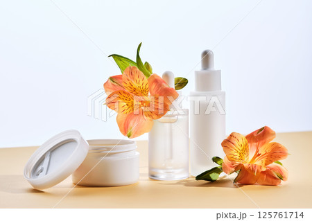 Two serums and a cream in a jar with lily flowers on a beige background. Two serums and a cream in a jar with lily flowers on a beige background. 125761714