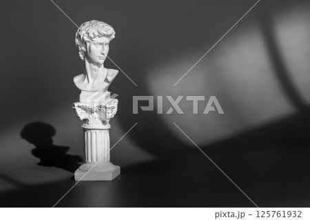 White marble head of young man, head of famous statue. Gypsum copy of ancient statue head on purple background with light and shadow 125761932